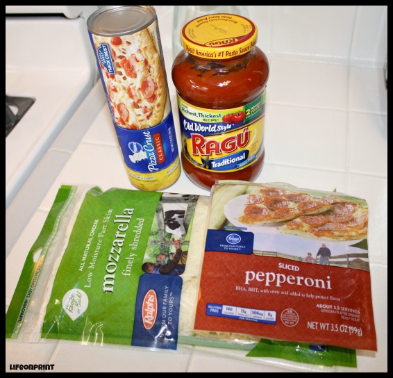 Pizza crust, jar of Ragu, mozzarella cheese, and sliced pepperoni on a countertop. 