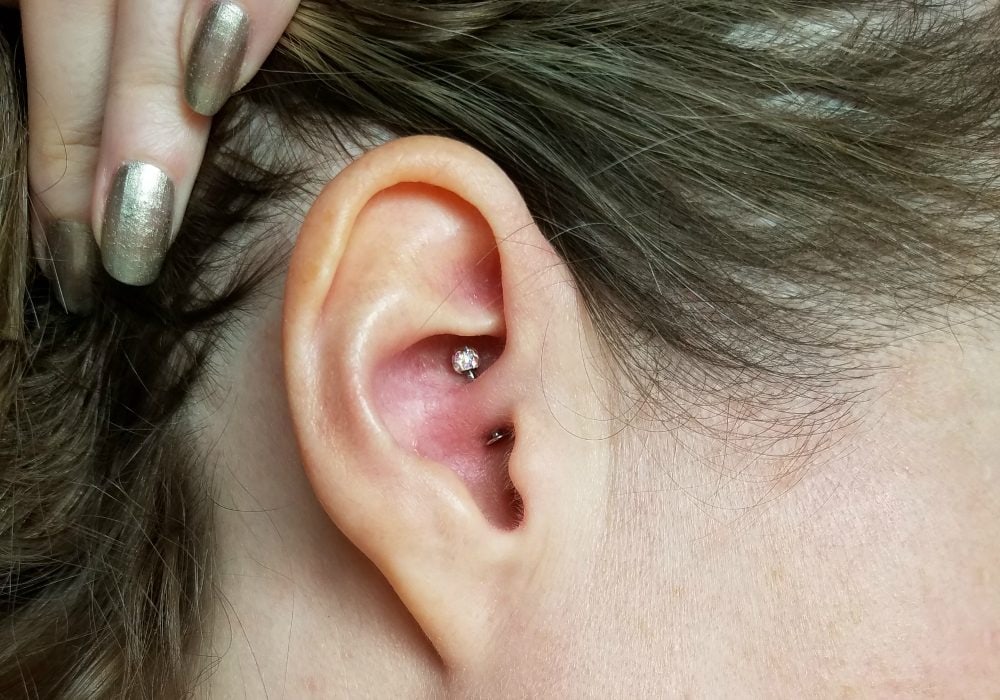 Holding hair back to see the daith piercing in an ear.