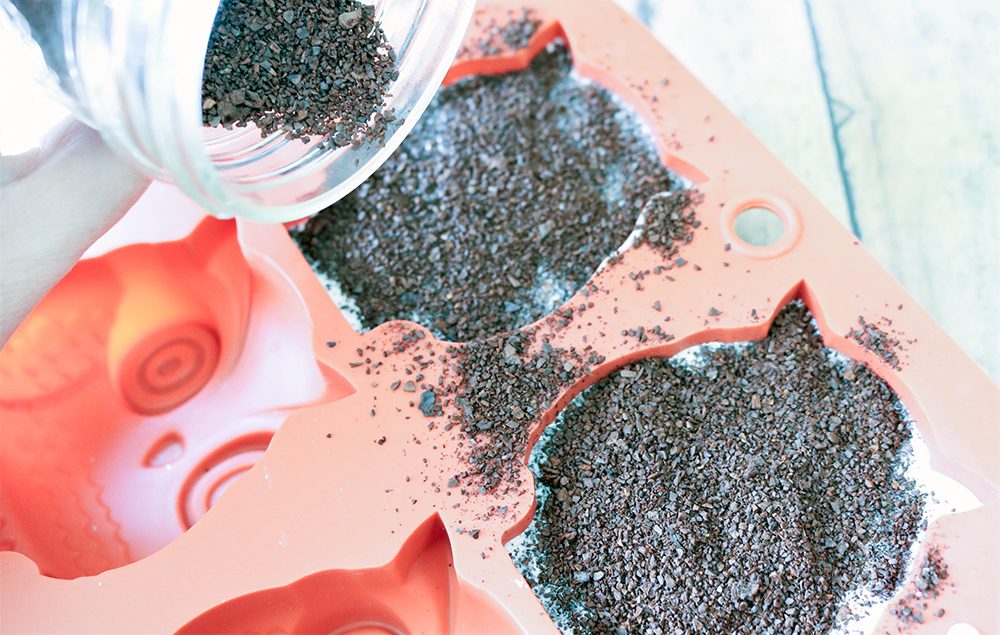 Pouring coffee grounds on top of soap in owl molds. 