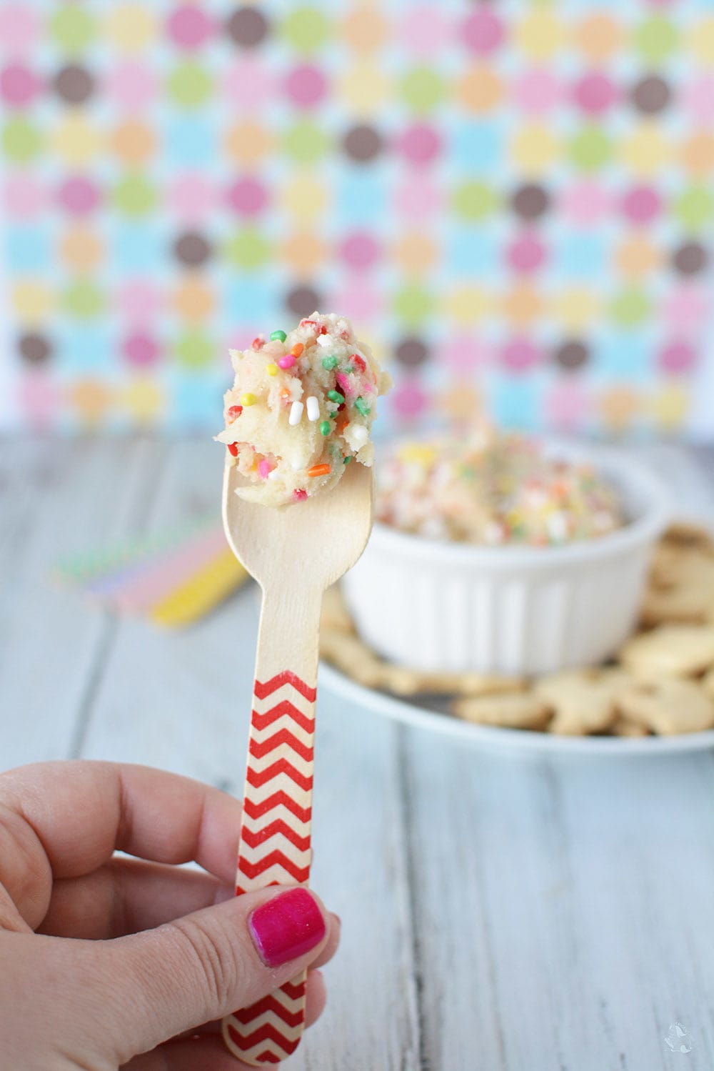 Rainbow cookie dough with sprinkles on a wooden spoon.