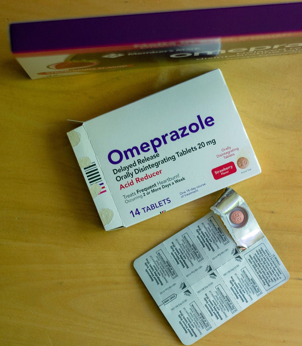 Box of heartburn medicine with a pill showing in the package sitting on a table. 