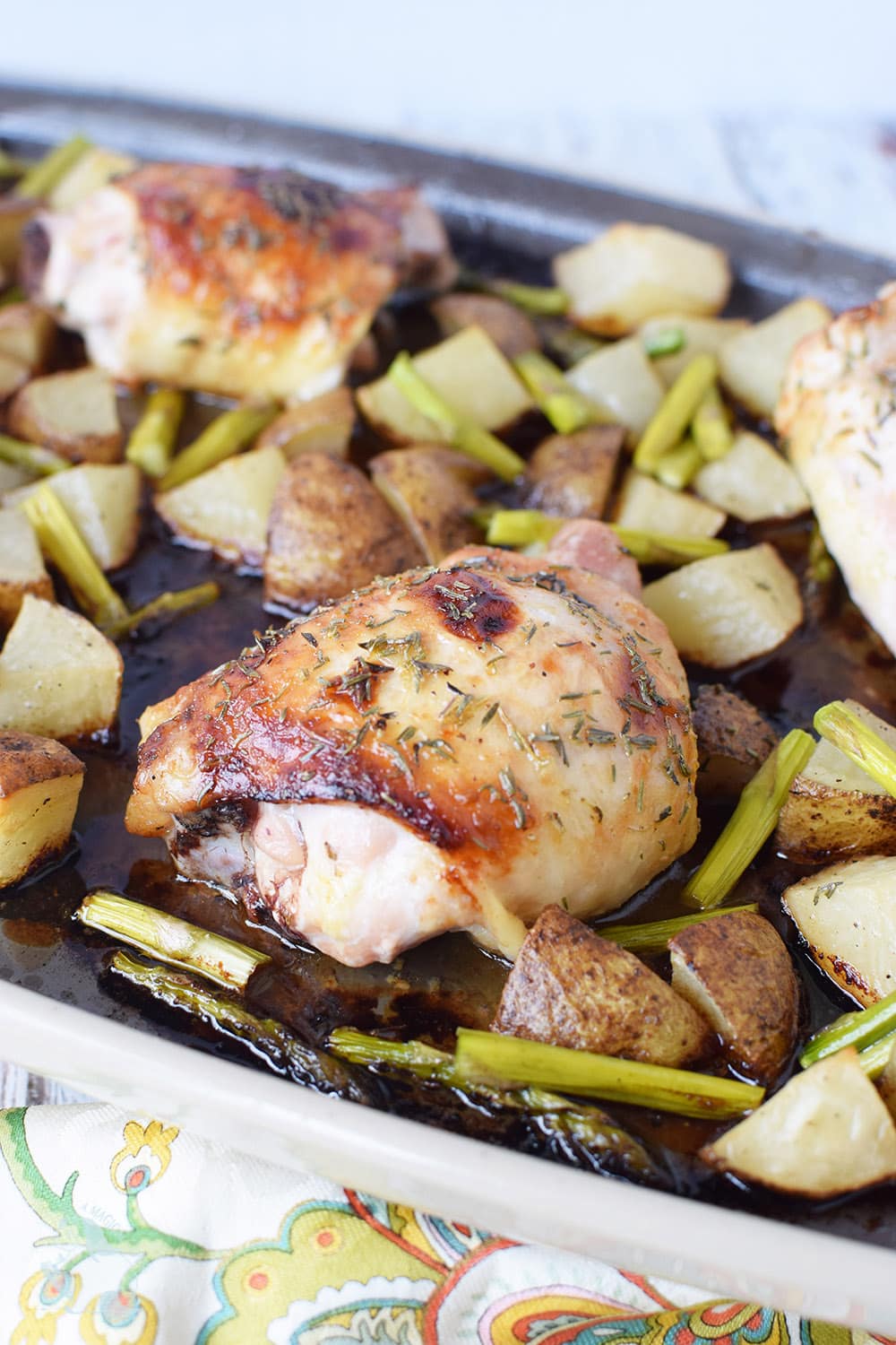 Baked chicken thighs topped with herbs on a sheet pan with veggies. 