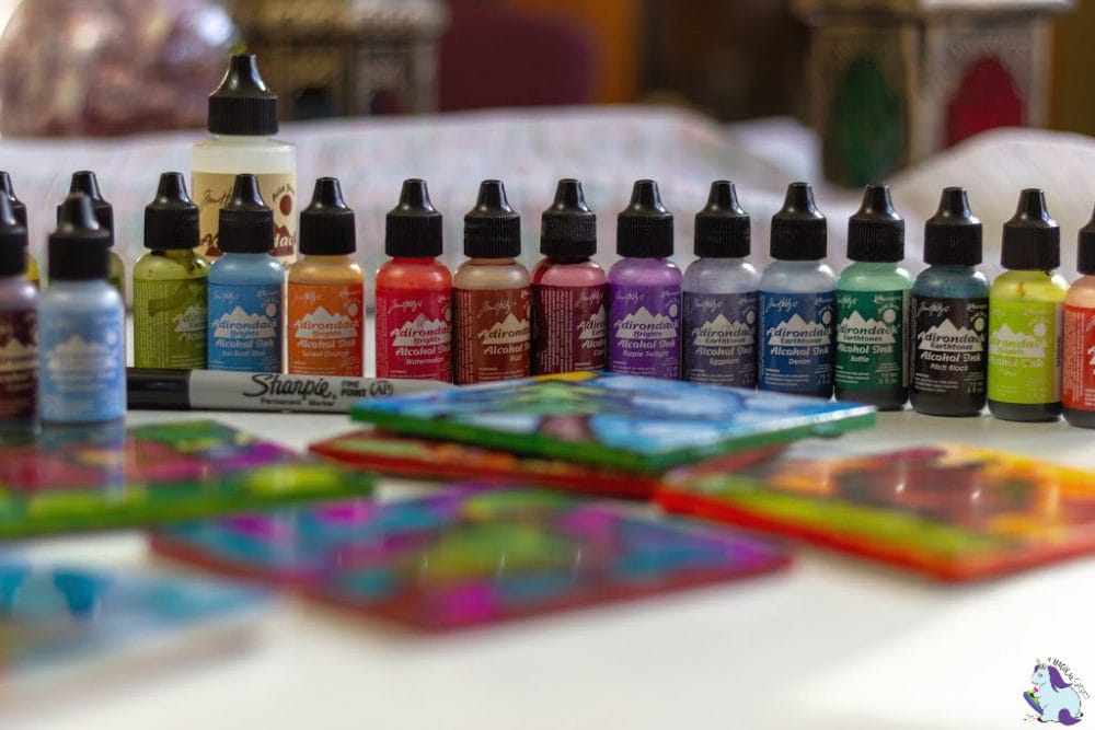 Adirondack Alcohol Ink bottles lined up by tiles on a table. 