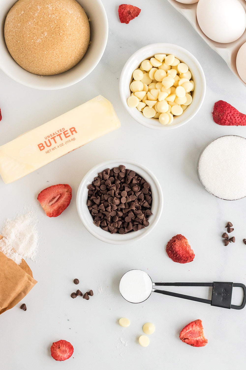 Brown sugar, eggs, chocolate chips, butter, and other ingredients for cookies in bowls. 