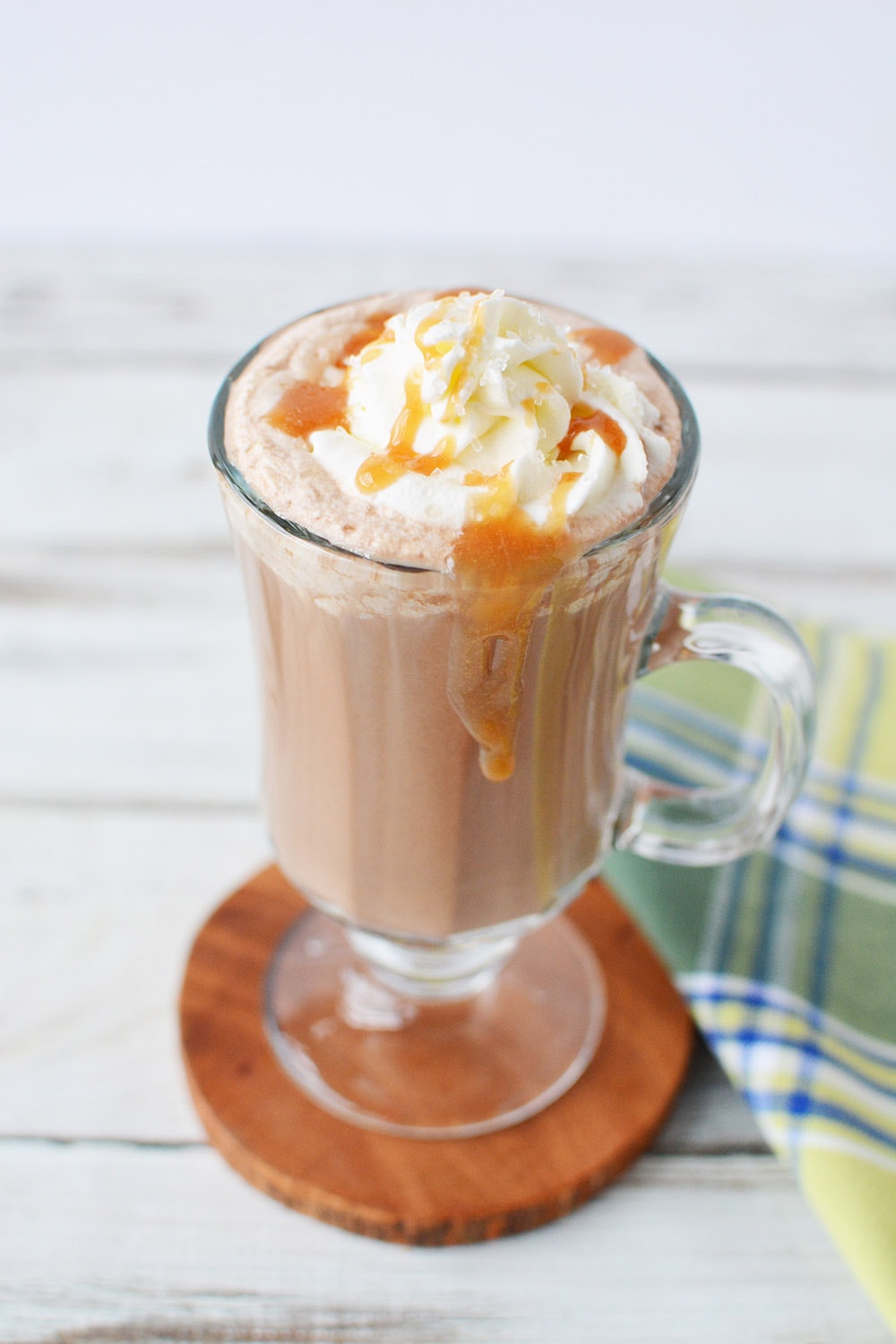 Coffee drink topped with whipped cream and caramel in a glass mug.