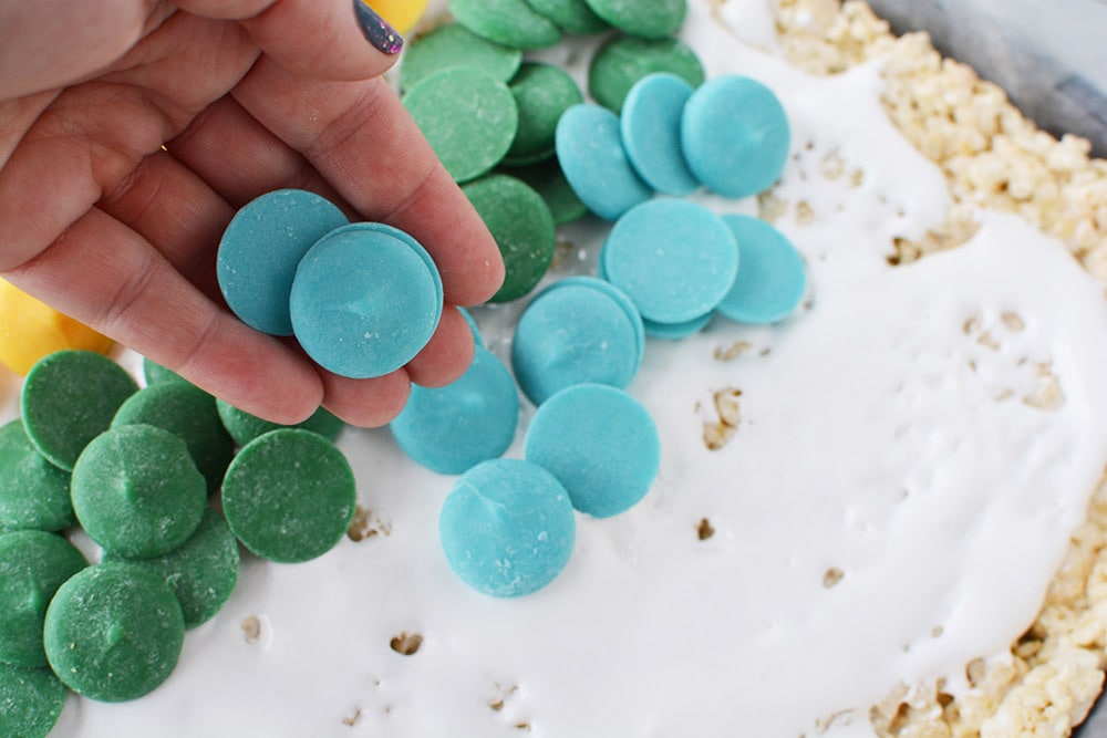 Adding candy melts onto rice cereal in a baking sheet. 