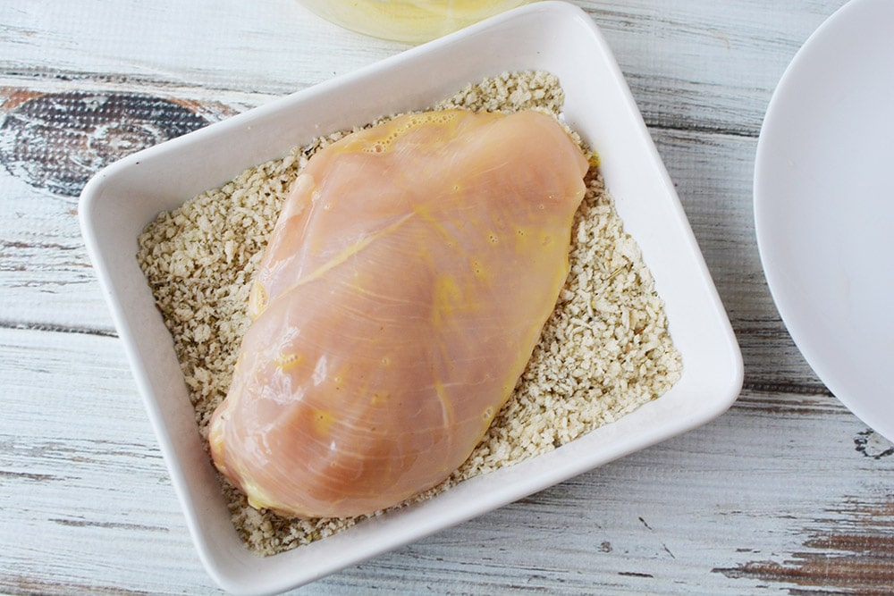 Dipping egg washed chicken into a bowl of bread crumbs.