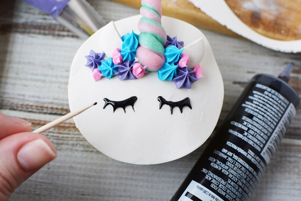 Drawing eyes on a unicorn cupcake with black frosting.