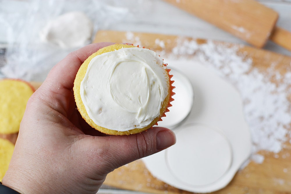 White frosting on a cupcake above a board with candy clay on it.