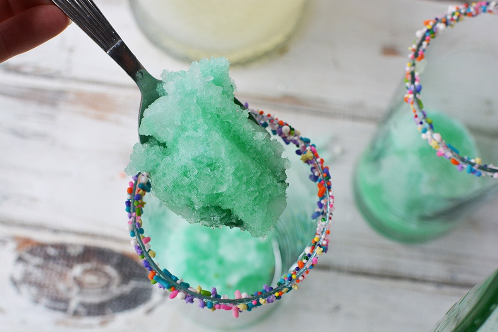 Spoon filled with icy green lemonade above a glass. 