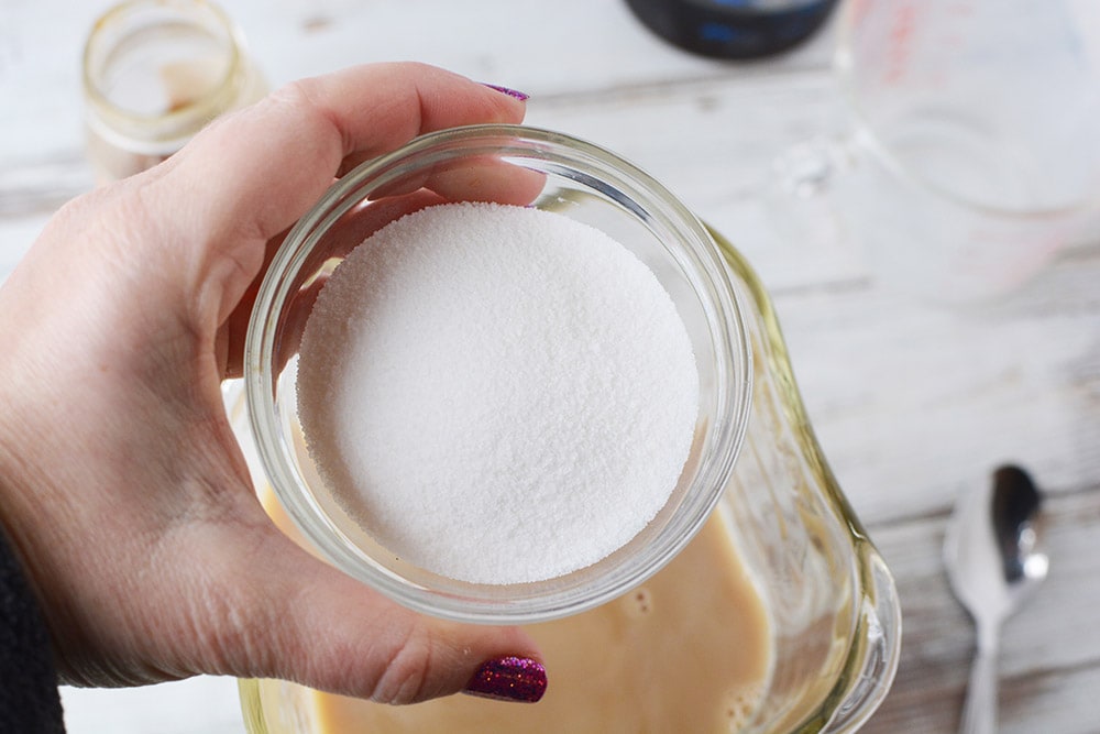 Holding a bowl of sugar above a blender. 