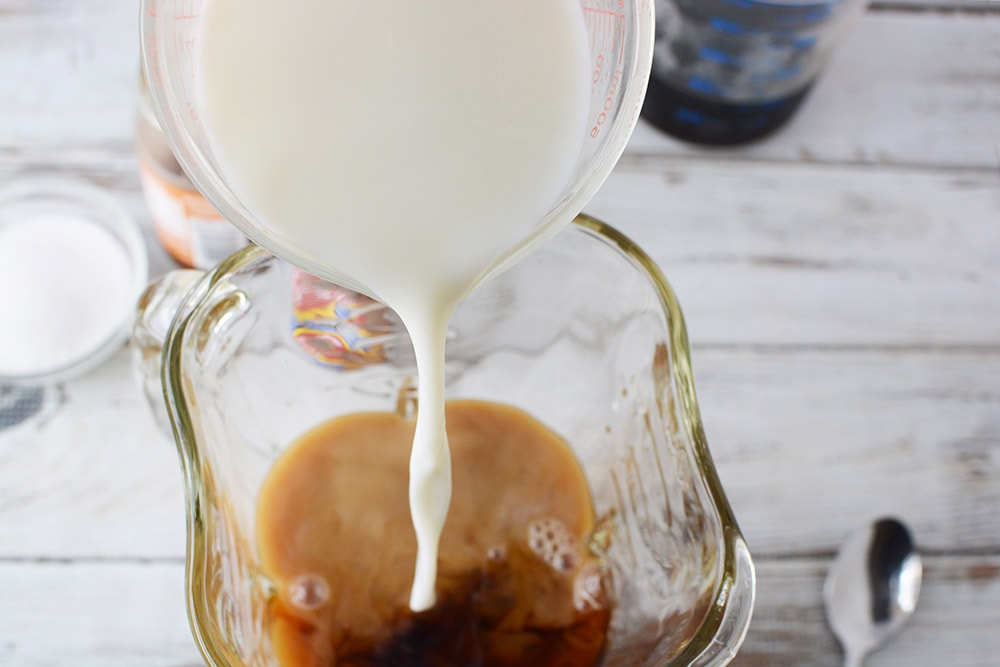 Pouring milk into a blender that has coffee in it. 
