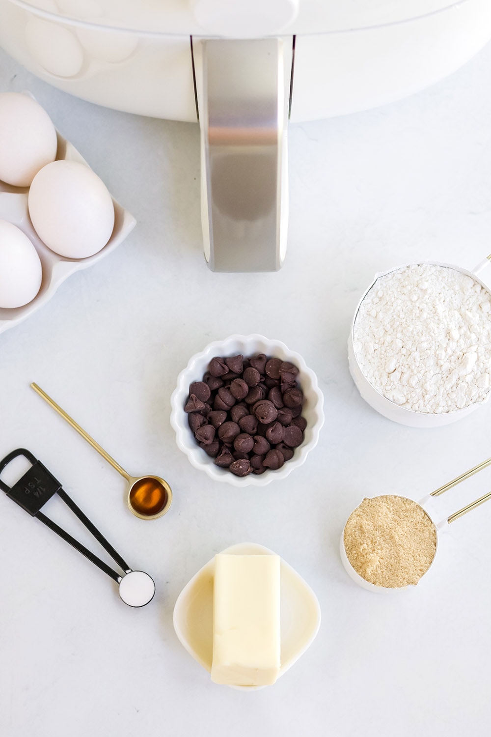 Eggs, chocolate chips, flour, butter, and vanilla in front of an air fryer.
