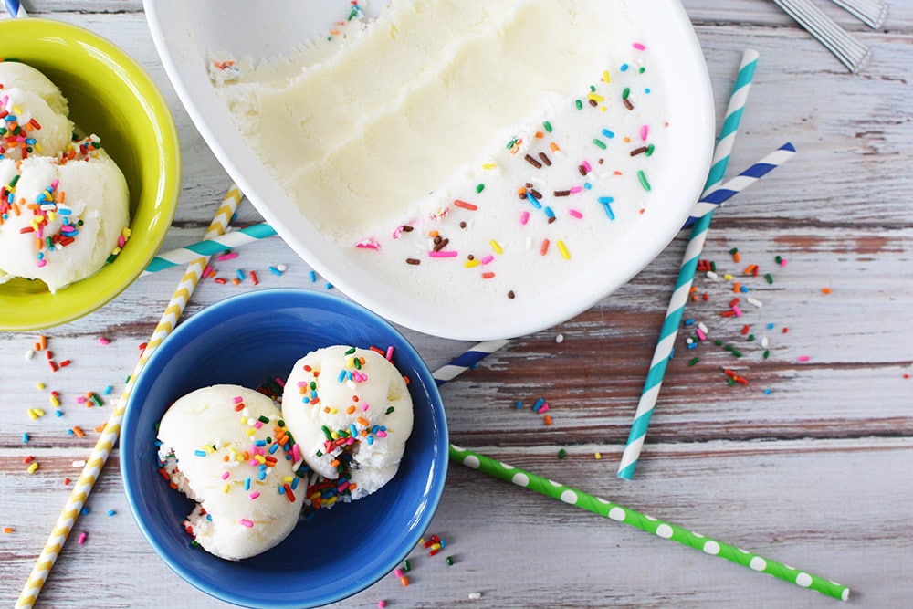 Birthday cake ice cream in a blue bowl next to the scooped out dish.