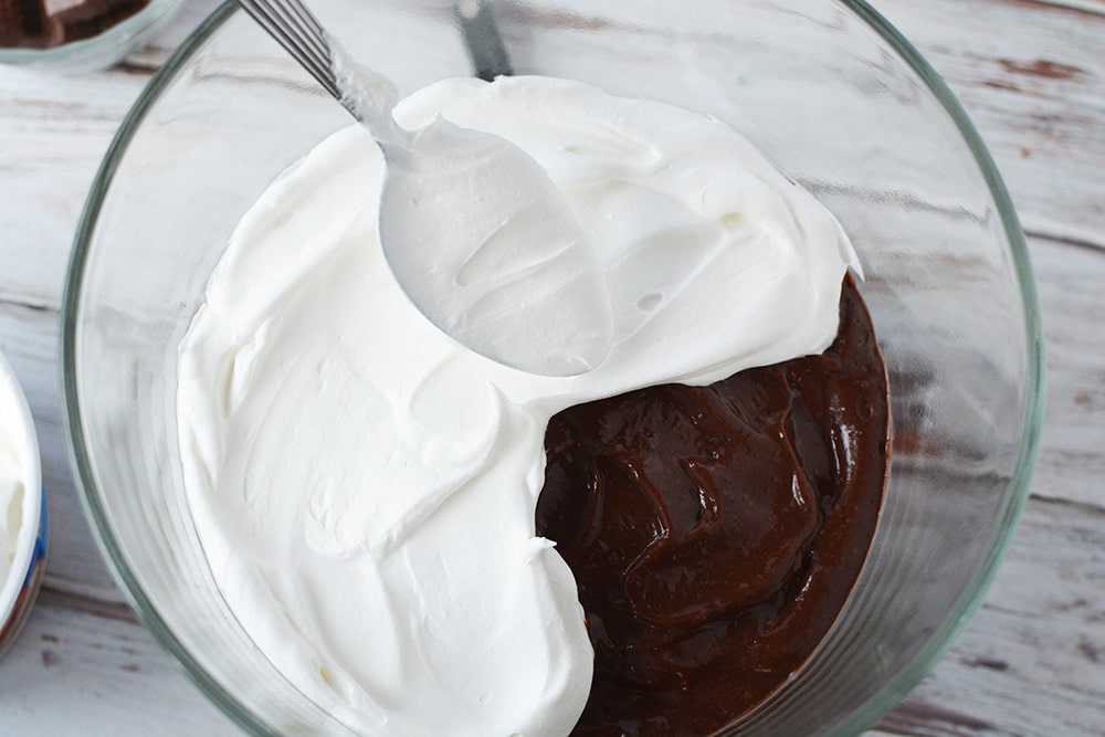 Spooning whipped cream on top of pudding in a trifle bowl. 