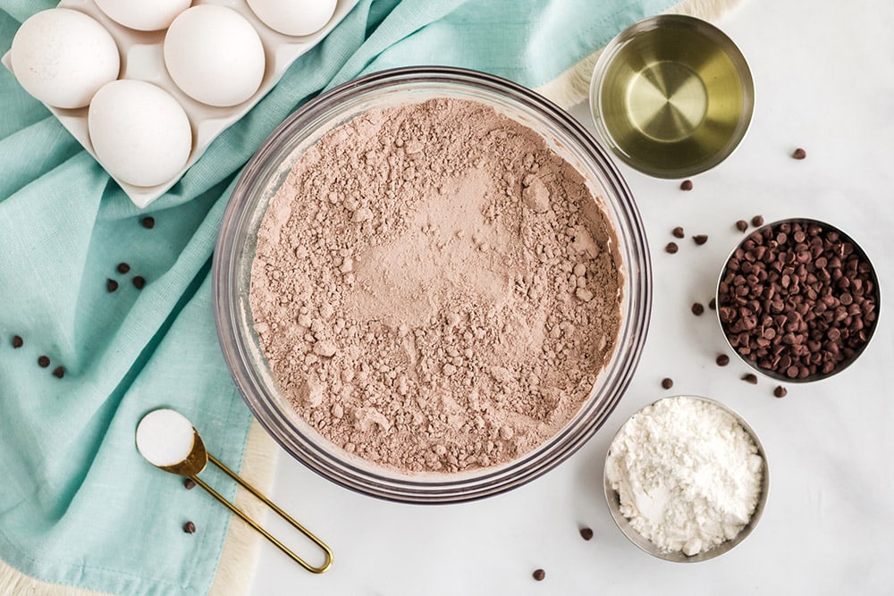 Brownie mix, chips, eggs, and other ingredients on a table.