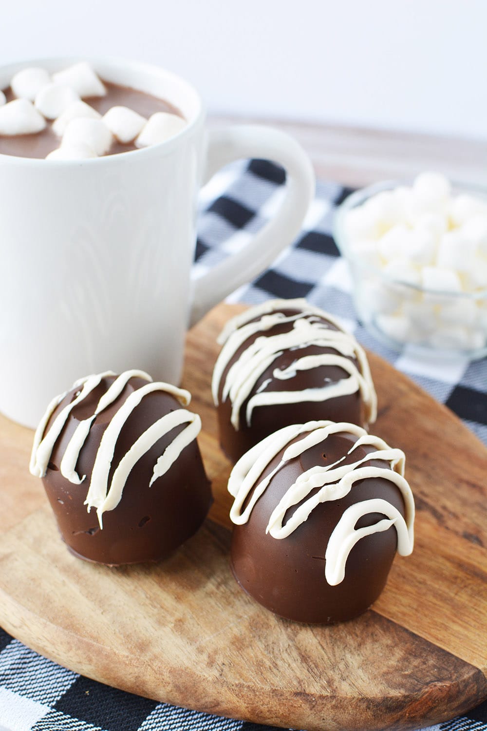 Three hot cocoa bombs on a board with a blue checked napkin on a table.
