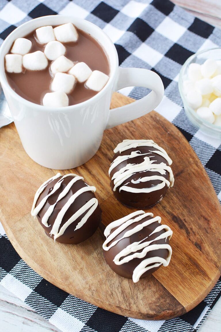 Three hot chocolate bombs on a board next to a mug.