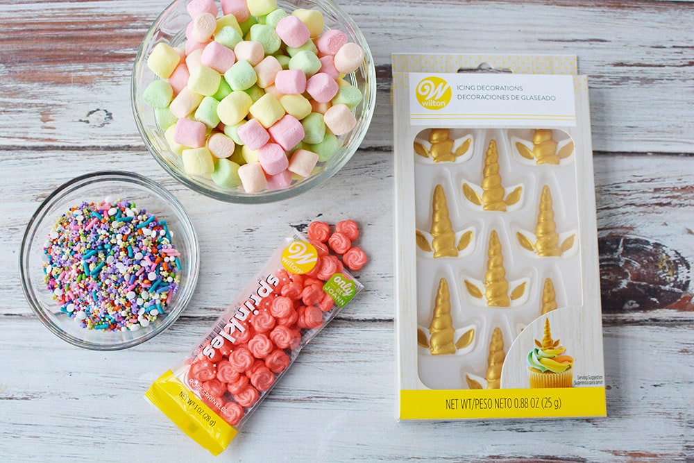 Colored marshmallows, gold horns, sprinkles, and candy flowers on a table. 