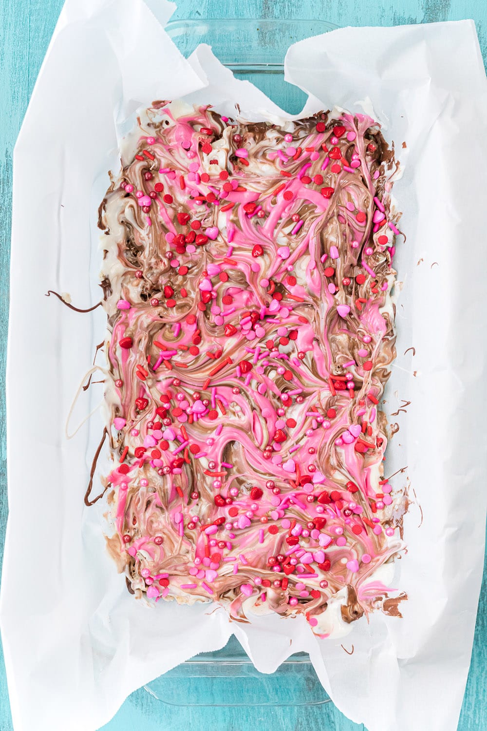 Valentine sprinkles on top of chocolate bark candy in a pan.