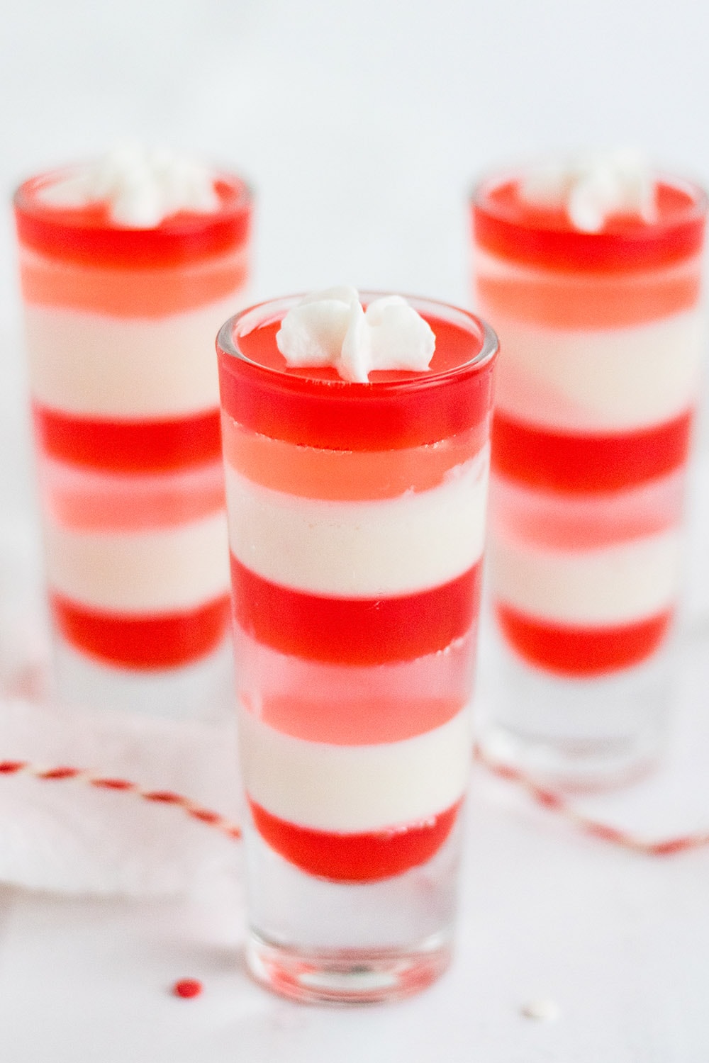 Three shooter glasses with layers of white, pink, and red gelatin.