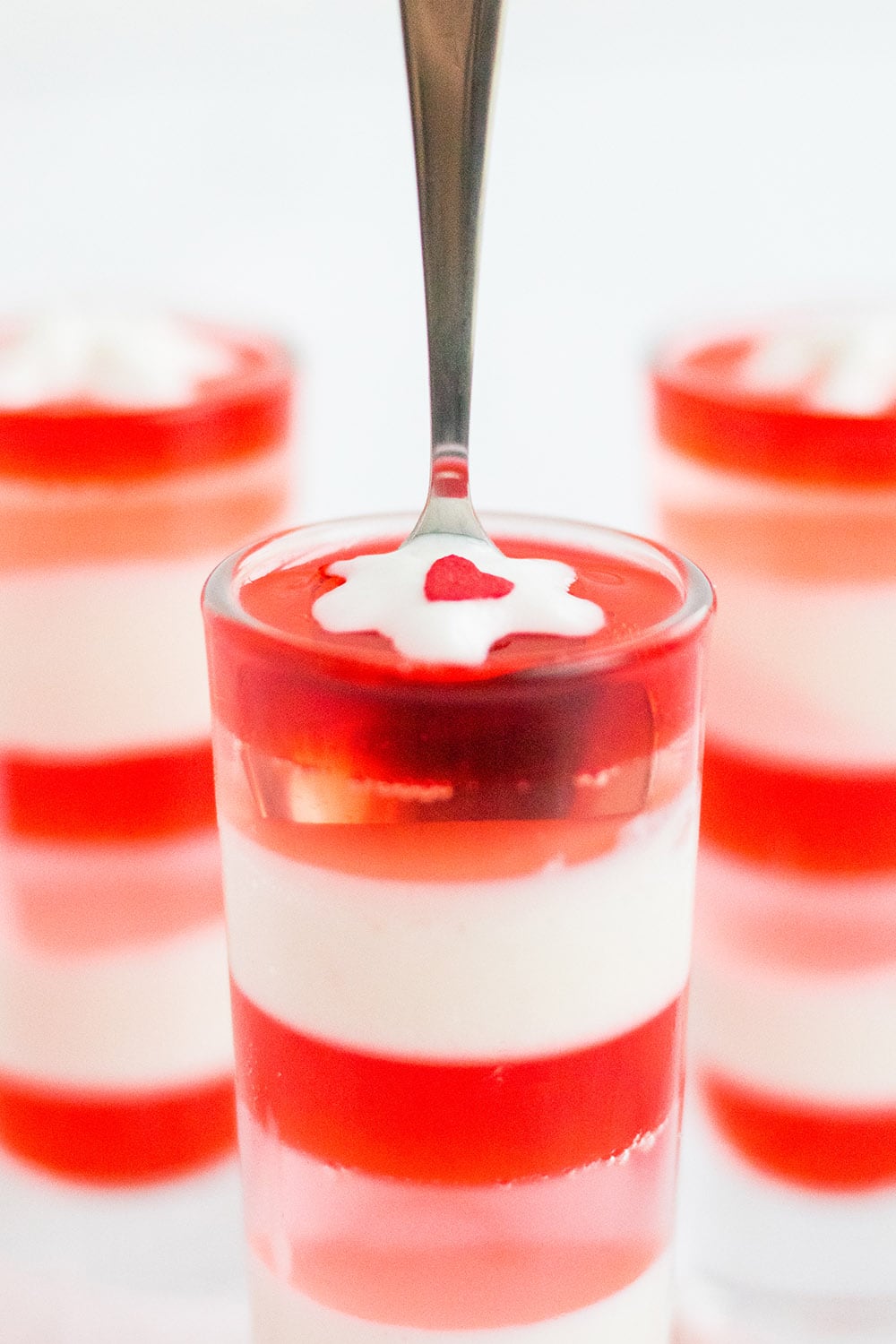 Spoon in a glass of layered gelatin with pink, red, and white layers.