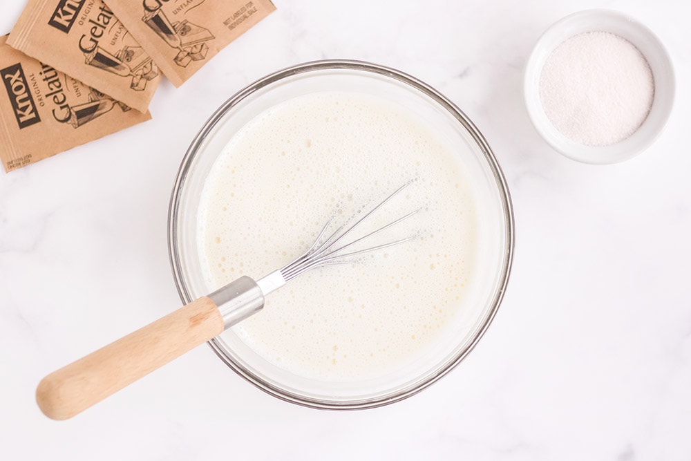 White gelatin in a bowl with a whisk in it. 