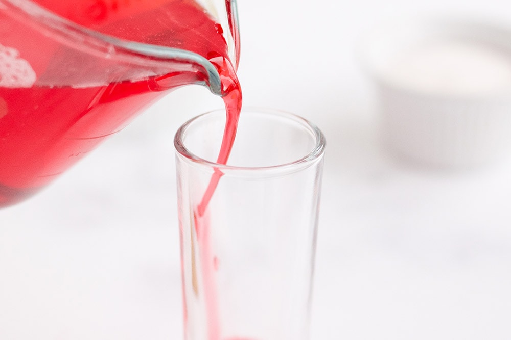 Pouring red gelatin into dessert cup.