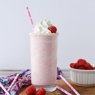Pink cotton candy blended drink in a glass topped with whipped cream and raspberries.