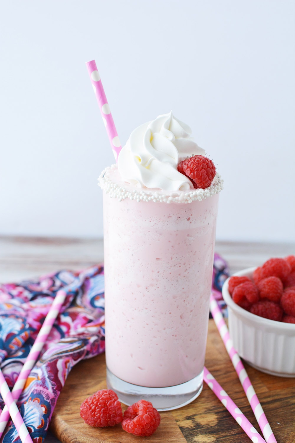 Glass of cotton candy frappuccino topped with whipped cream and raspberry and a pink straw. 