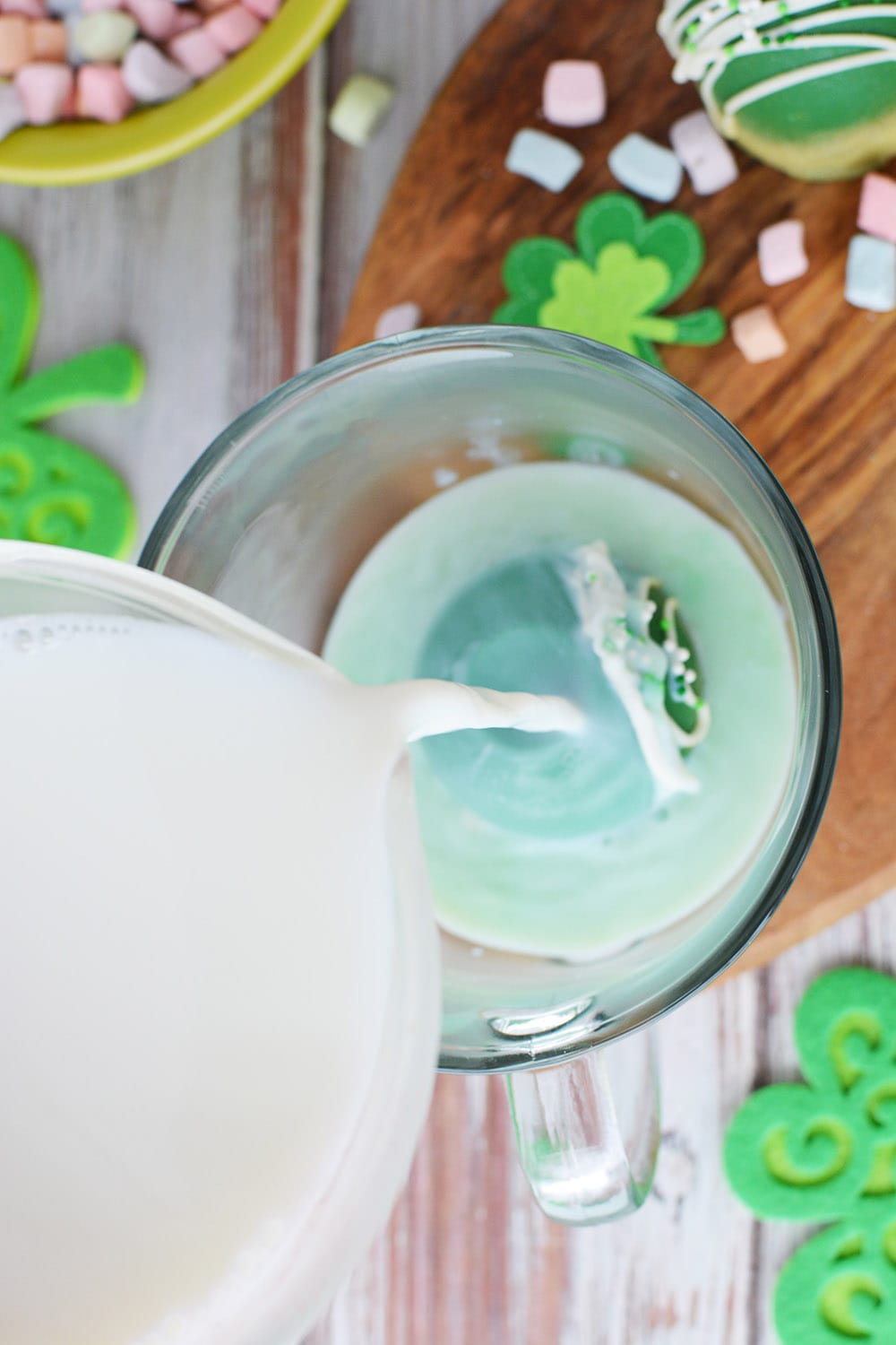 Pouring hot milk over a green cocoa bomb in a glass mug.