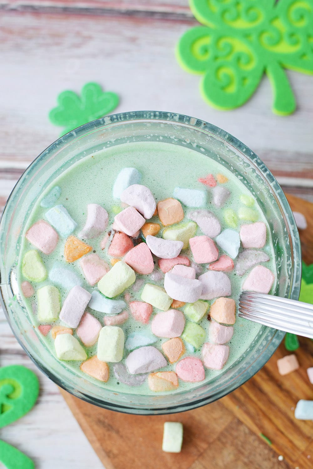Green hot chocolate with rainbow marshmallows in a glass mug.