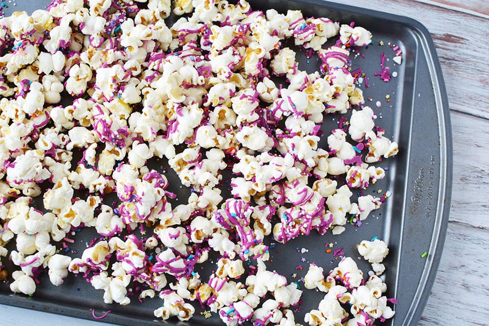 Baking sheet of popcorn with candy drizzle on it.