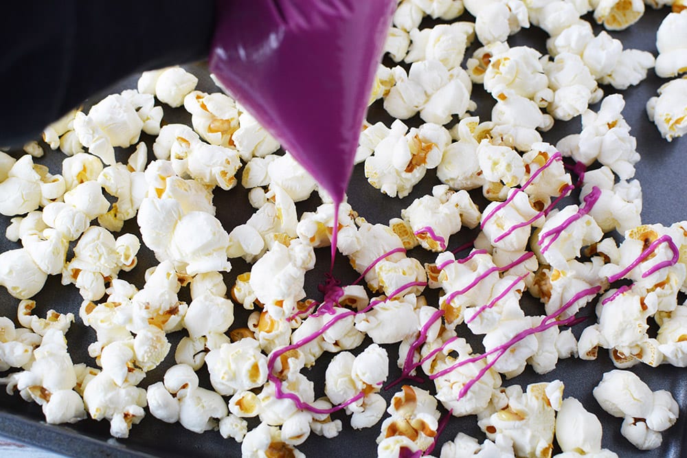 Drizzling pink chocolate onto plain popcorn.