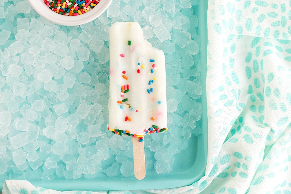 Bite taken out of a cake mix popsicle on ice. 