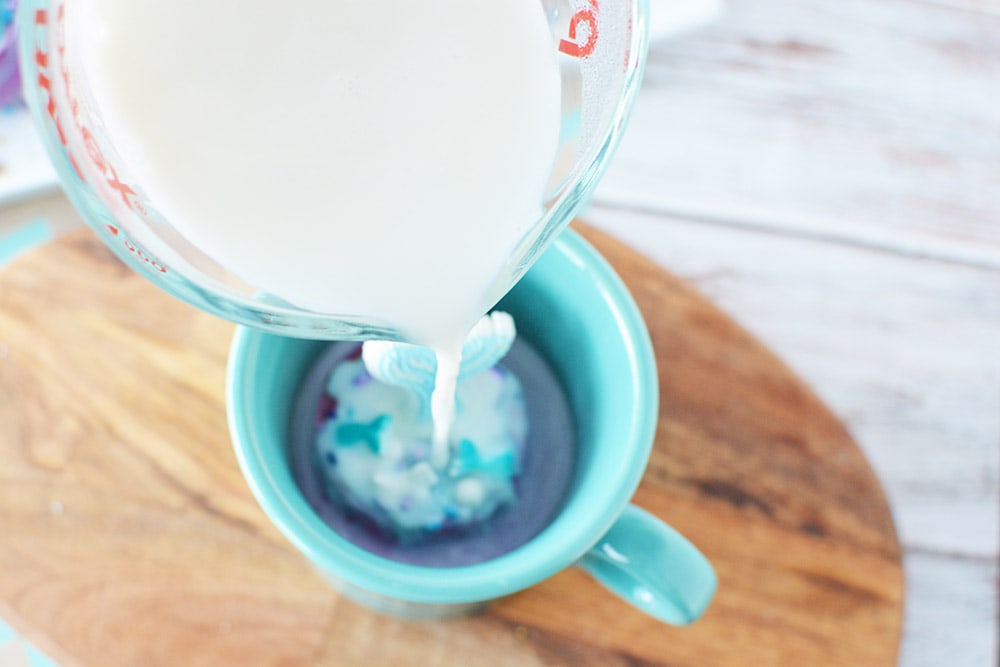Pouring hot milk onto a hot chocolate bomb in a mug.