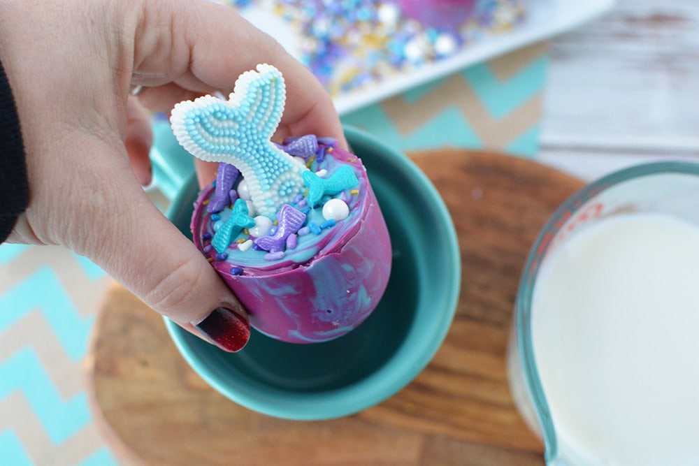Dropping a mermaid hot chocolate bomb into a mug.