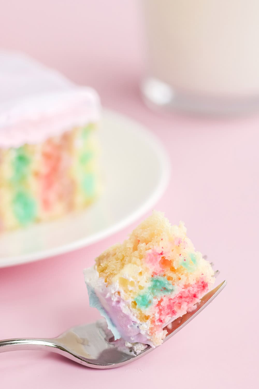 Fork with cake on it with a slice of poke cake on a plate.