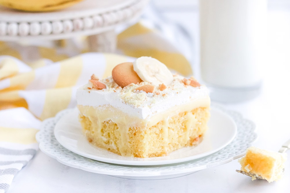 Yellow cake on a white plate on a white table with bananas and cookies.