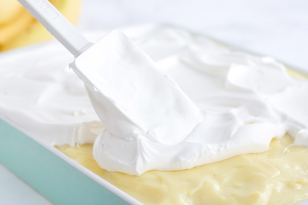 Spreading whipped topping on a cake with holes in it.