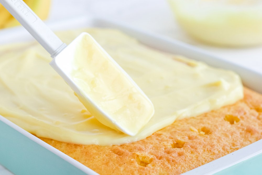 Spreading pudding on top of a cake with wholes in it.