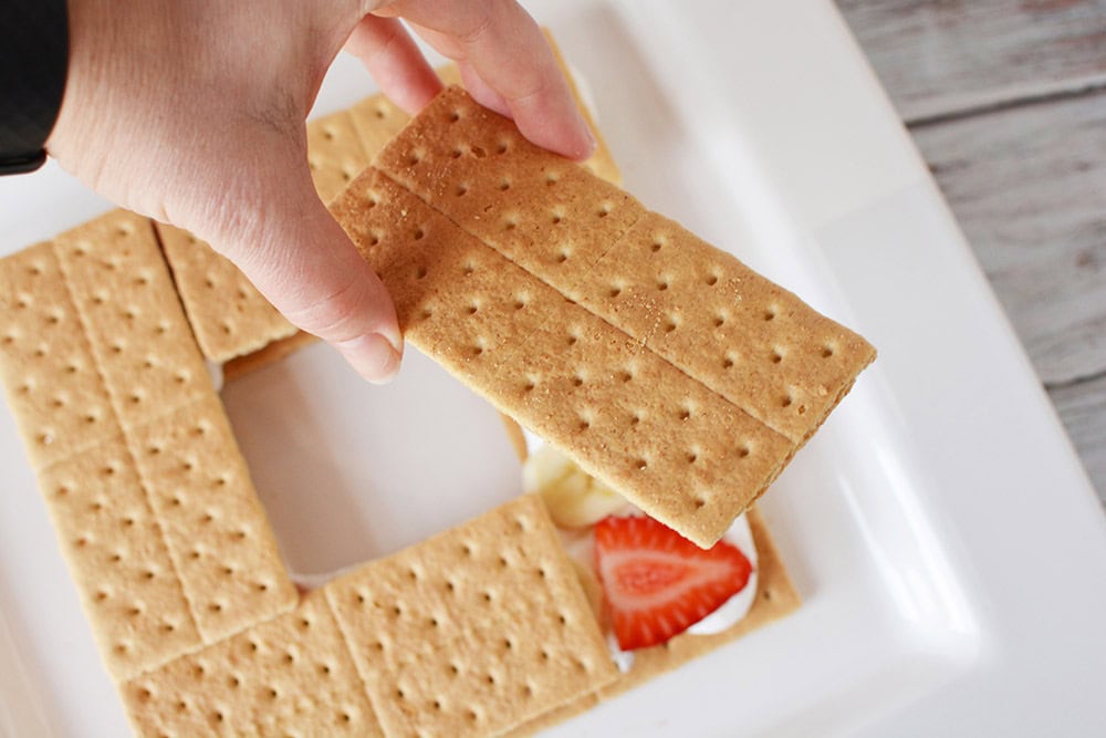 Stacking graham crackers on top of a strawberry.