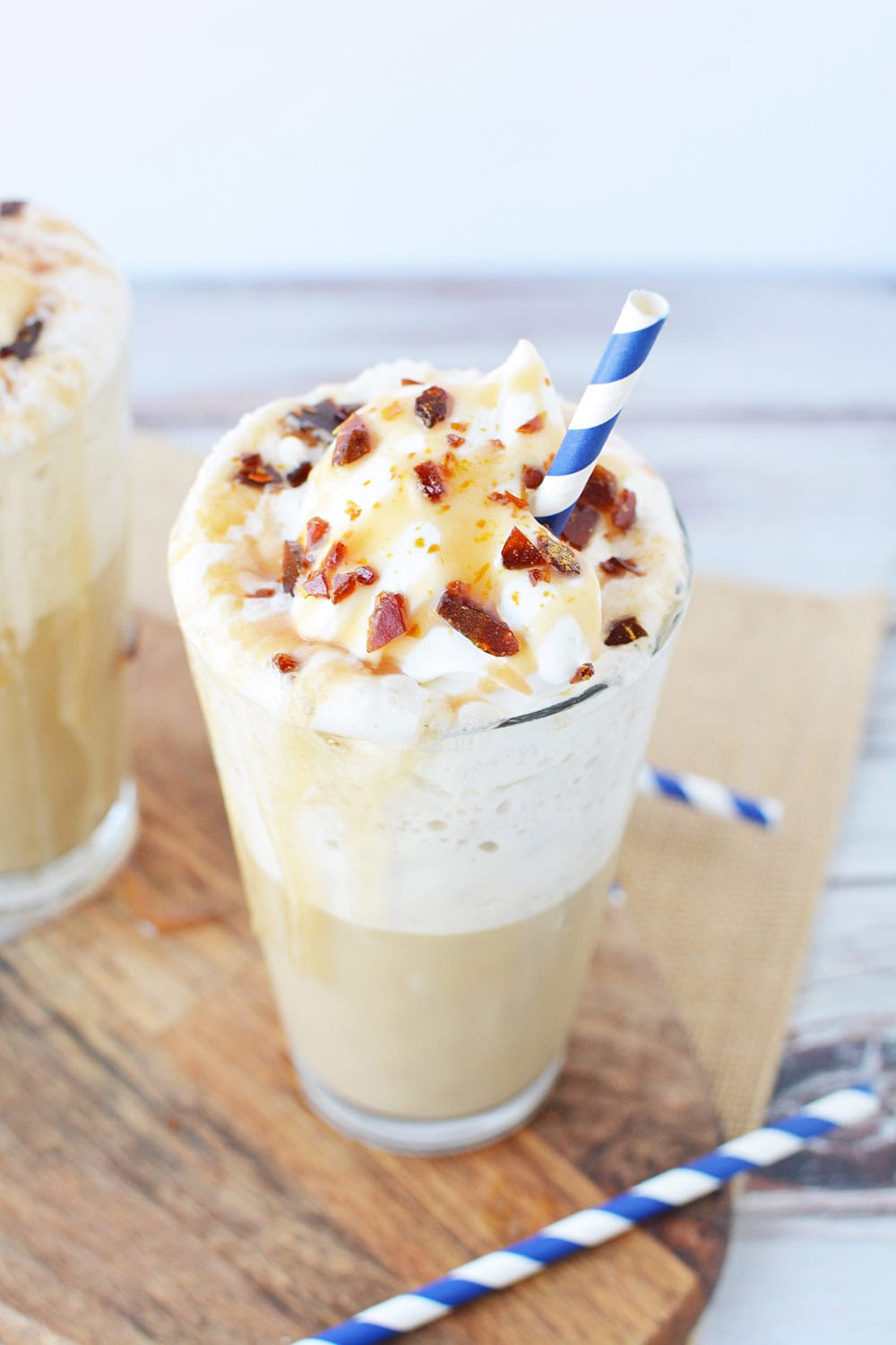 Caramel drink with whipped topping and sugar crunch with blue straw.