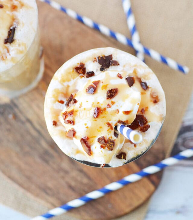 Overhead image of a caramel crunch frappuccino on a board with blue straws.
