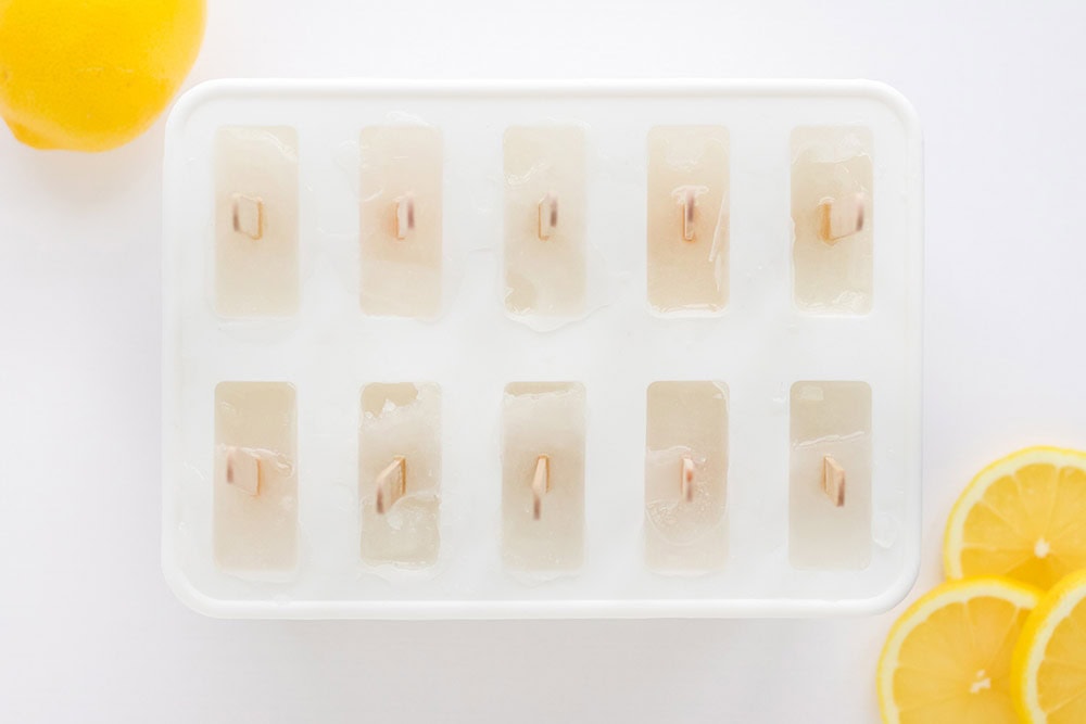 Frozen ice pops in the mold with lemon slices on the table.
