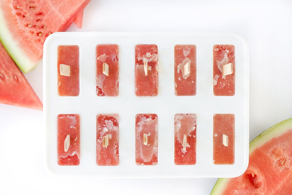 Popsicle mold with red liquid and popsicles sticks in it.