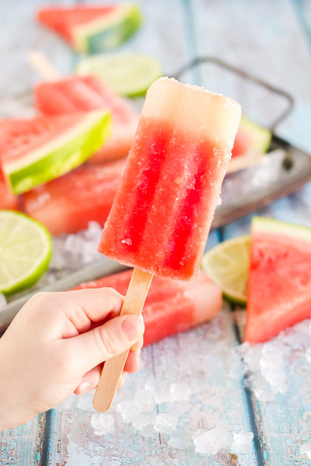 Holding a red popsicle with more pops in the back on a tray.
