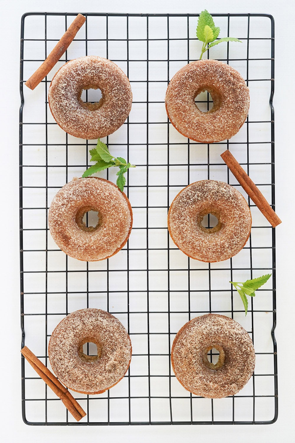 Donuts, cinnamon sticks, and green leaves on a wire rack.
