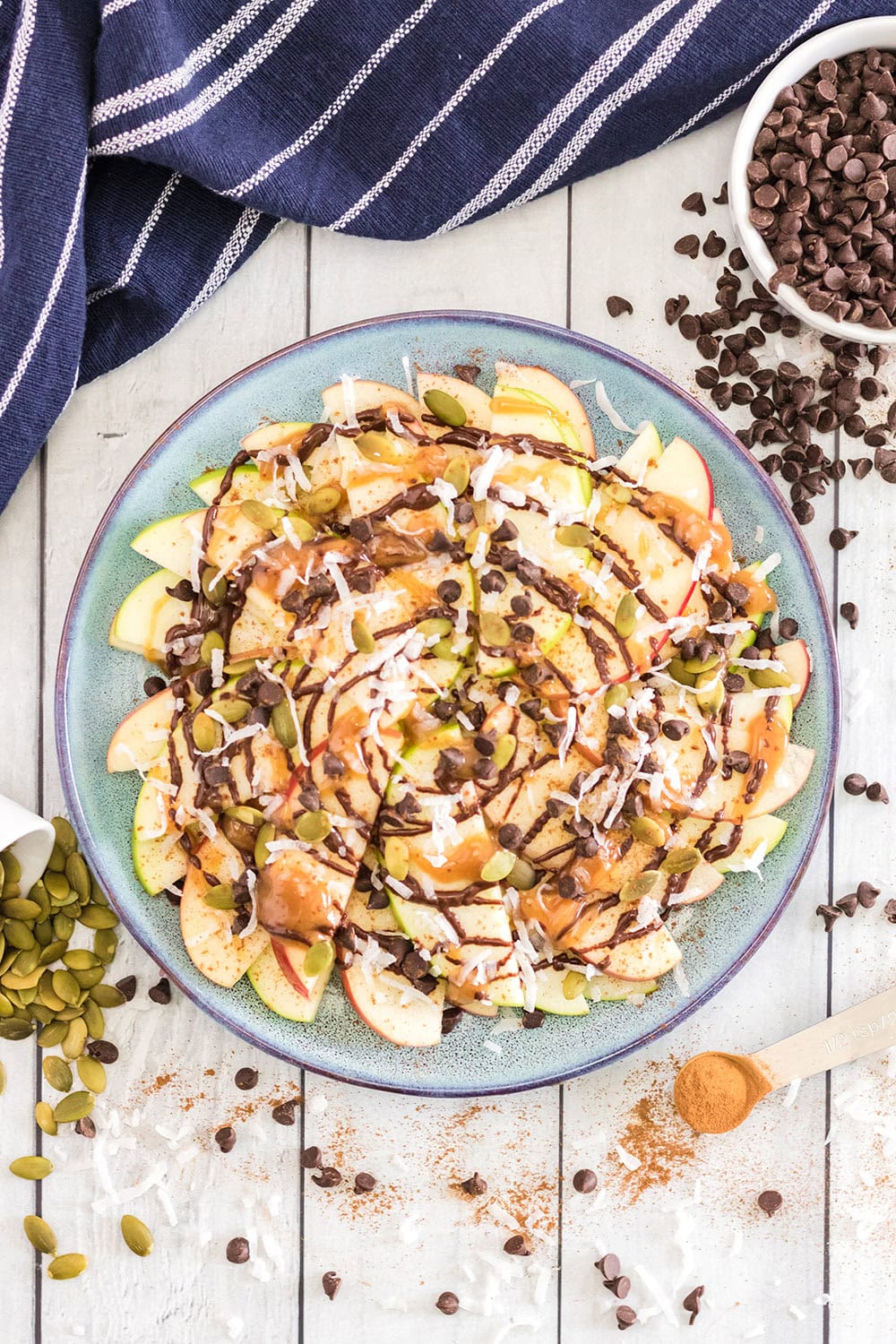 A blue plate filled with apple nachos and chips and other toppings on the table.