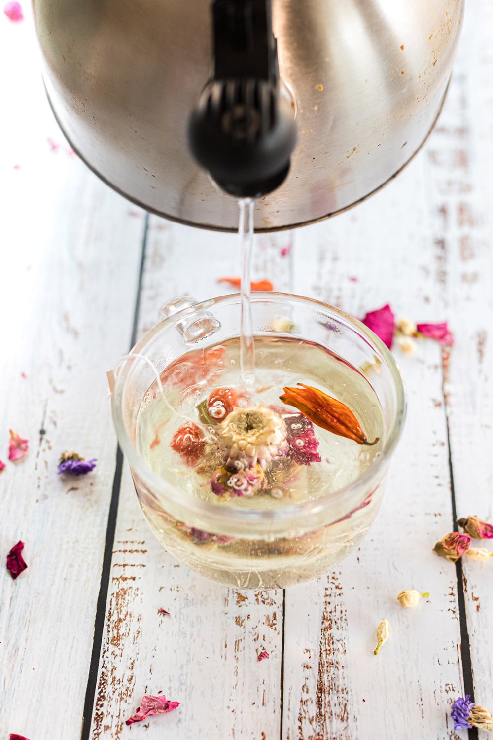 Pouring hot water over a flower tea drop in a mug.